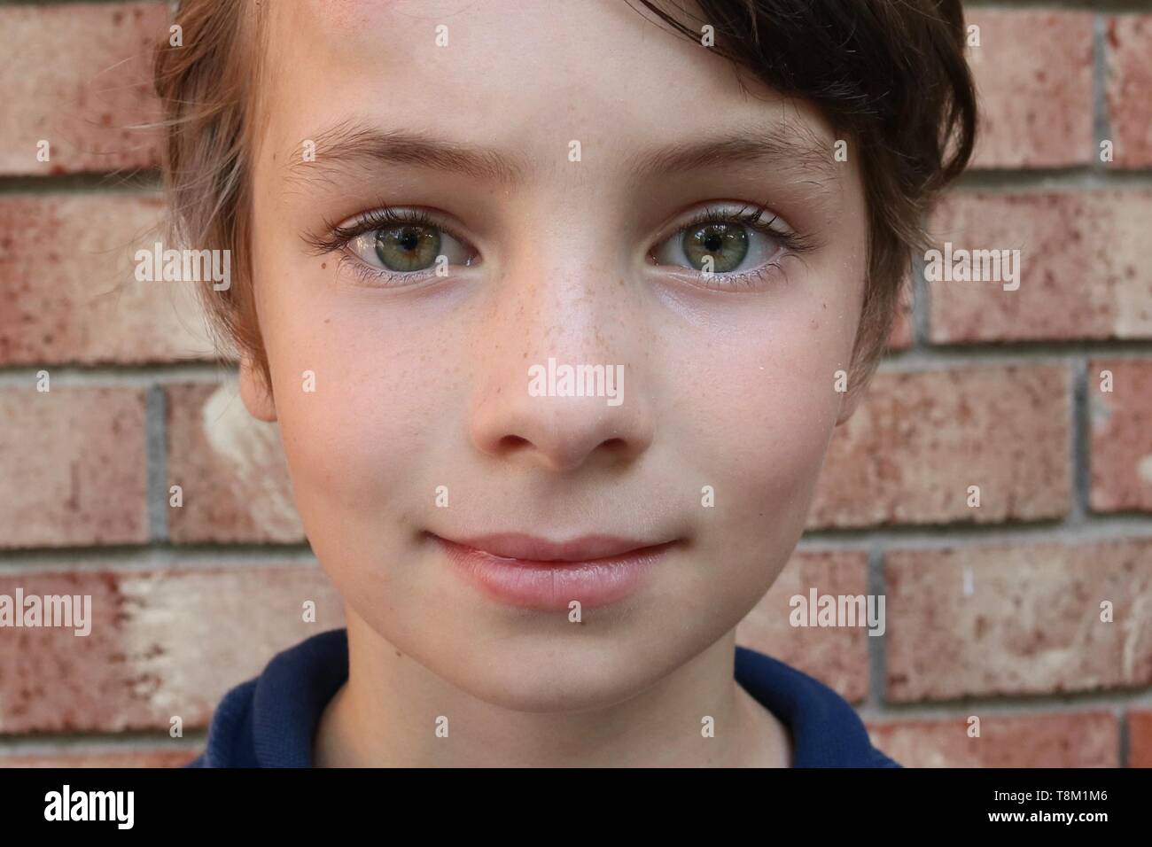 Portrait of a child with big green eyes in front of a brick wall Stock Photo