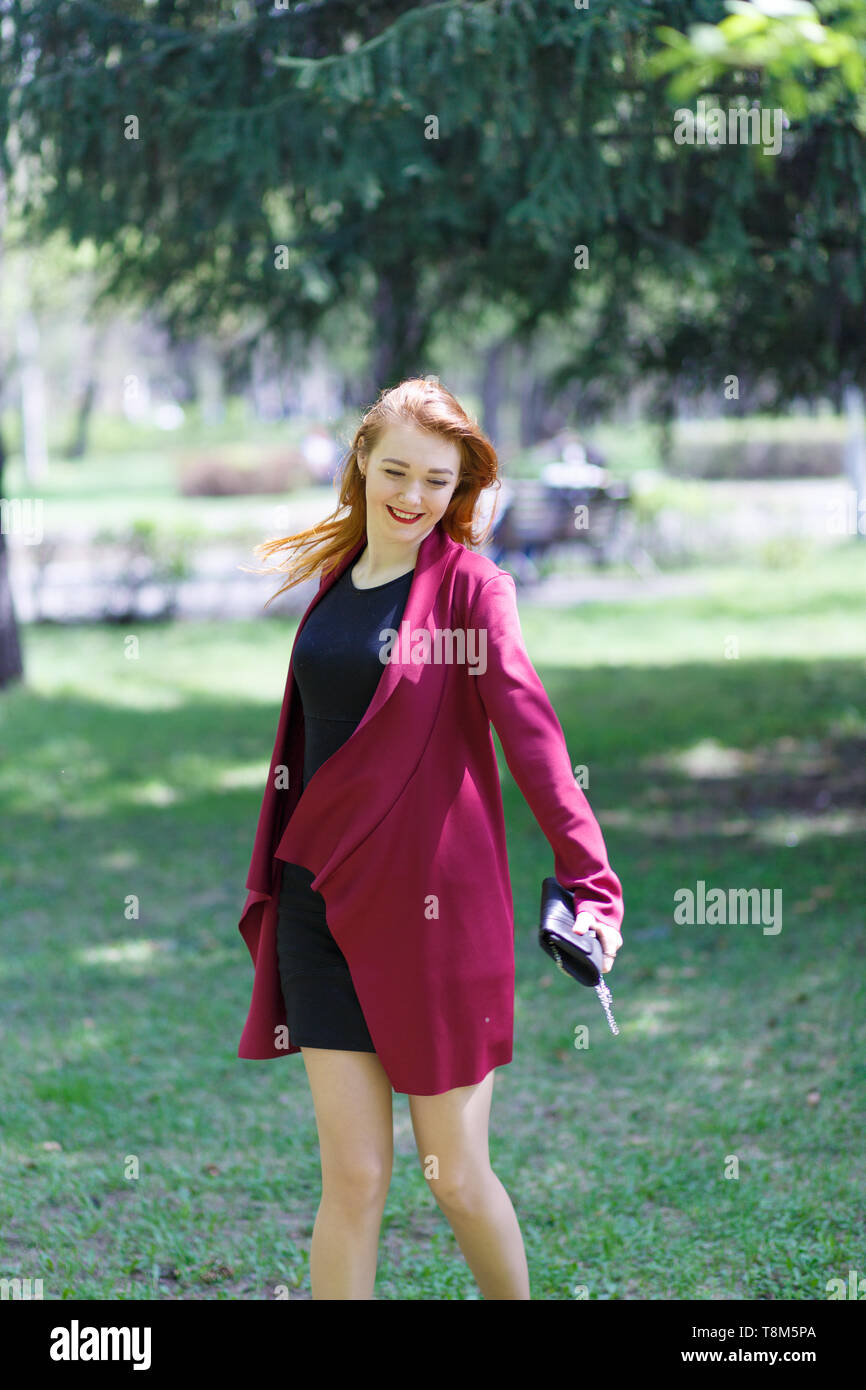 A young girl with red hair walks in the Park in a good mood. Happy girl ...