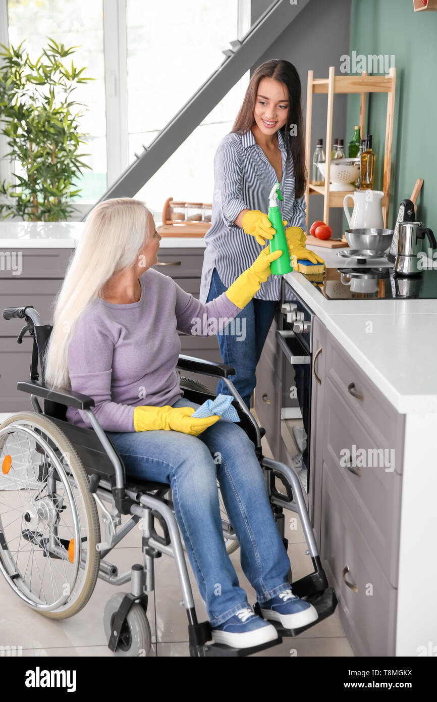Mature Woman In Wheelchair Cleaning Kitchen Together With Daughter