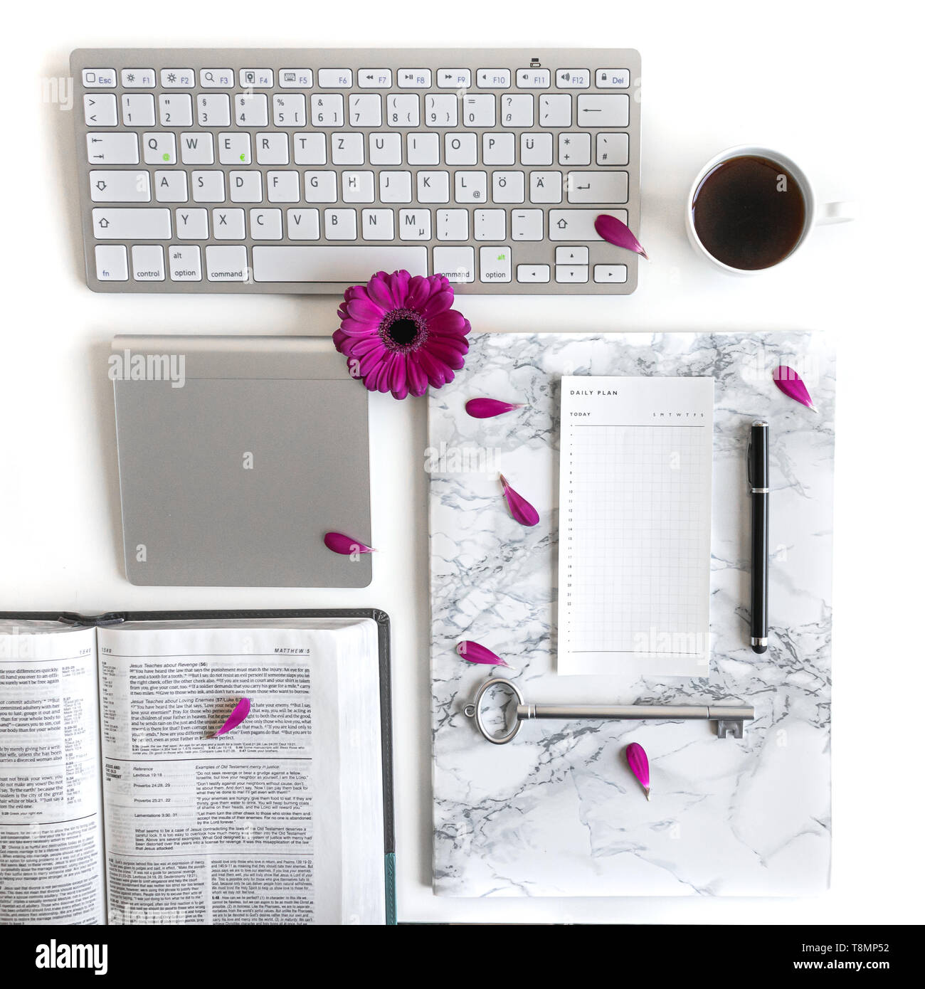 Flat lay open Bible or book and pink, purple, violet, red Gerbera flower on a white background. With pink petals, keyboard, black tea, to do list Stock Photo