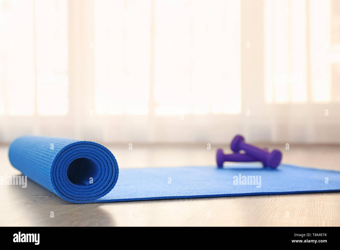 Yoga mat with dumbbells on light floor Stock Photo