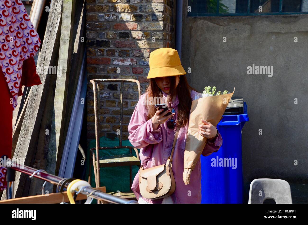 japanese tourist holding flowers looking at her phone columbia road london Stock Photo