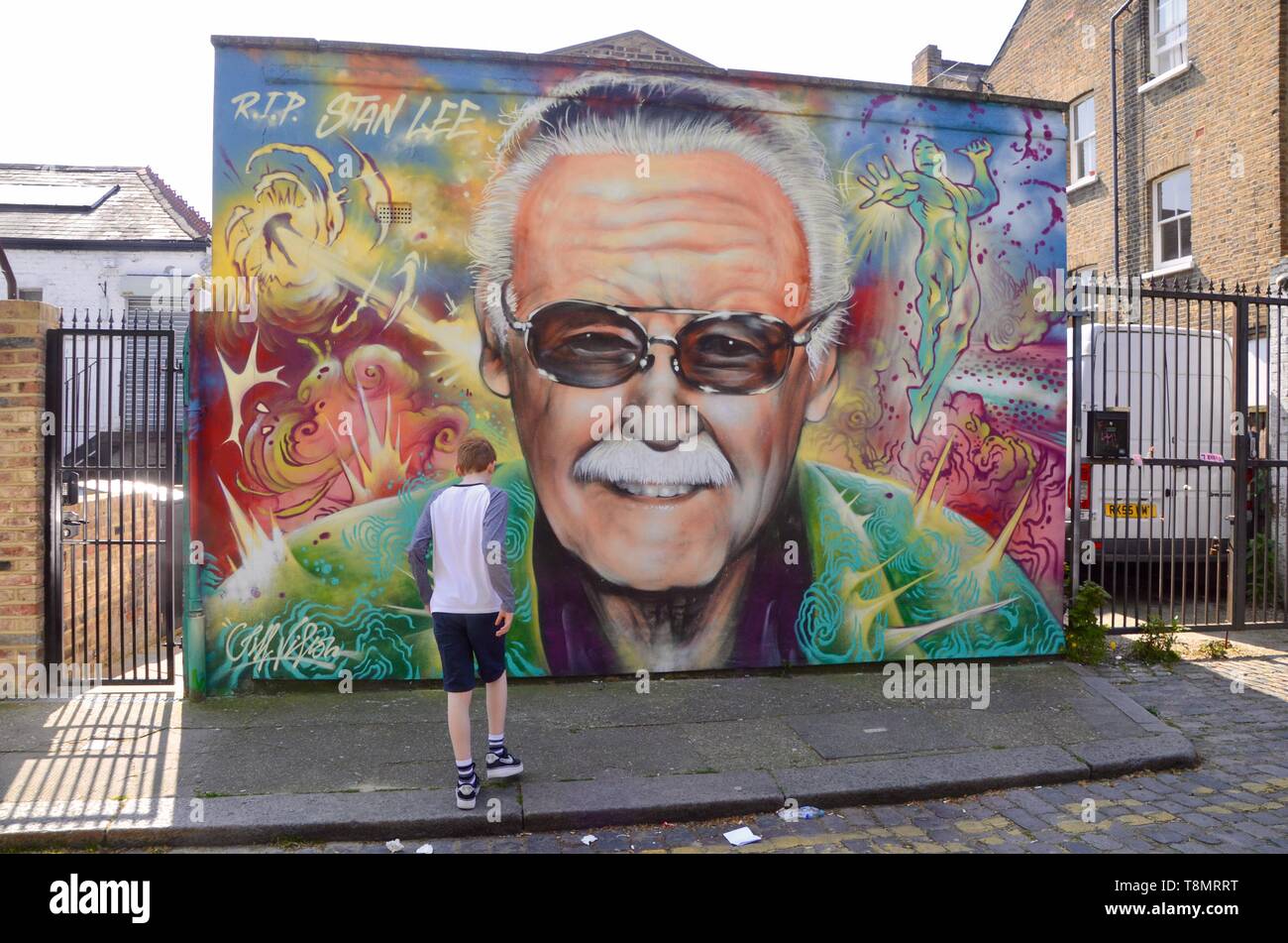 young boy stands in front of mural of stan lee off brick lane london uk Stock Photo