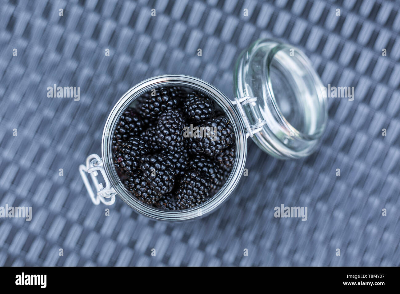 Fresh blackberries in a glass jar on a grey rattan surface viewed from above Stock Photo