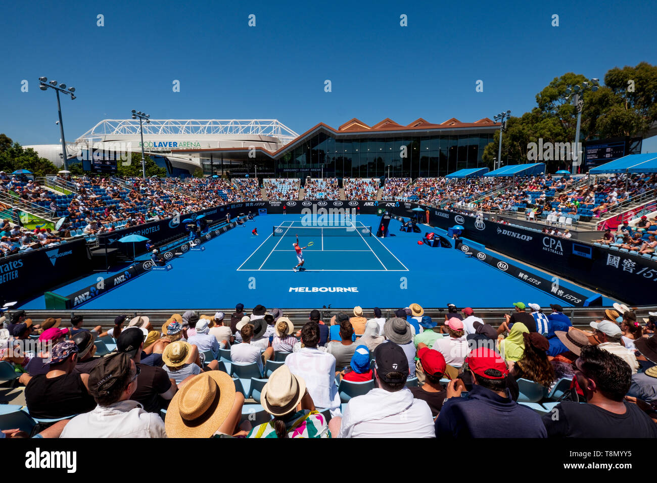 Fans attending a tennis match during the Australian Open on the outdoor Court 3 with Rod Laver Arena and Margaret Court Arena in the background. Stock Photo