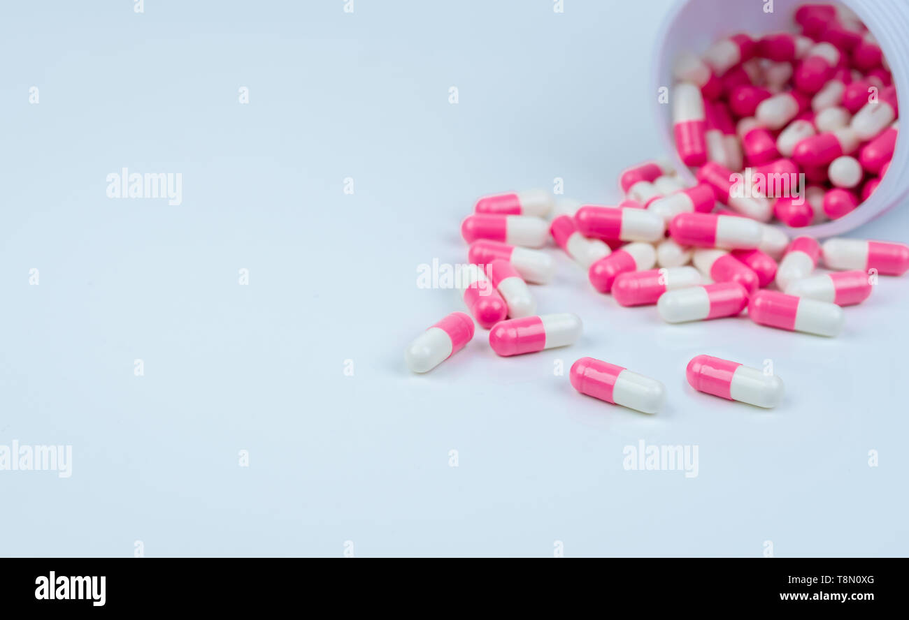 Pink-white capsule pills spread out of drug bottle. Antipsychotic drug. Capsule medicine for treatment depression. Anti-anxiety drug. Global health Stock Photo