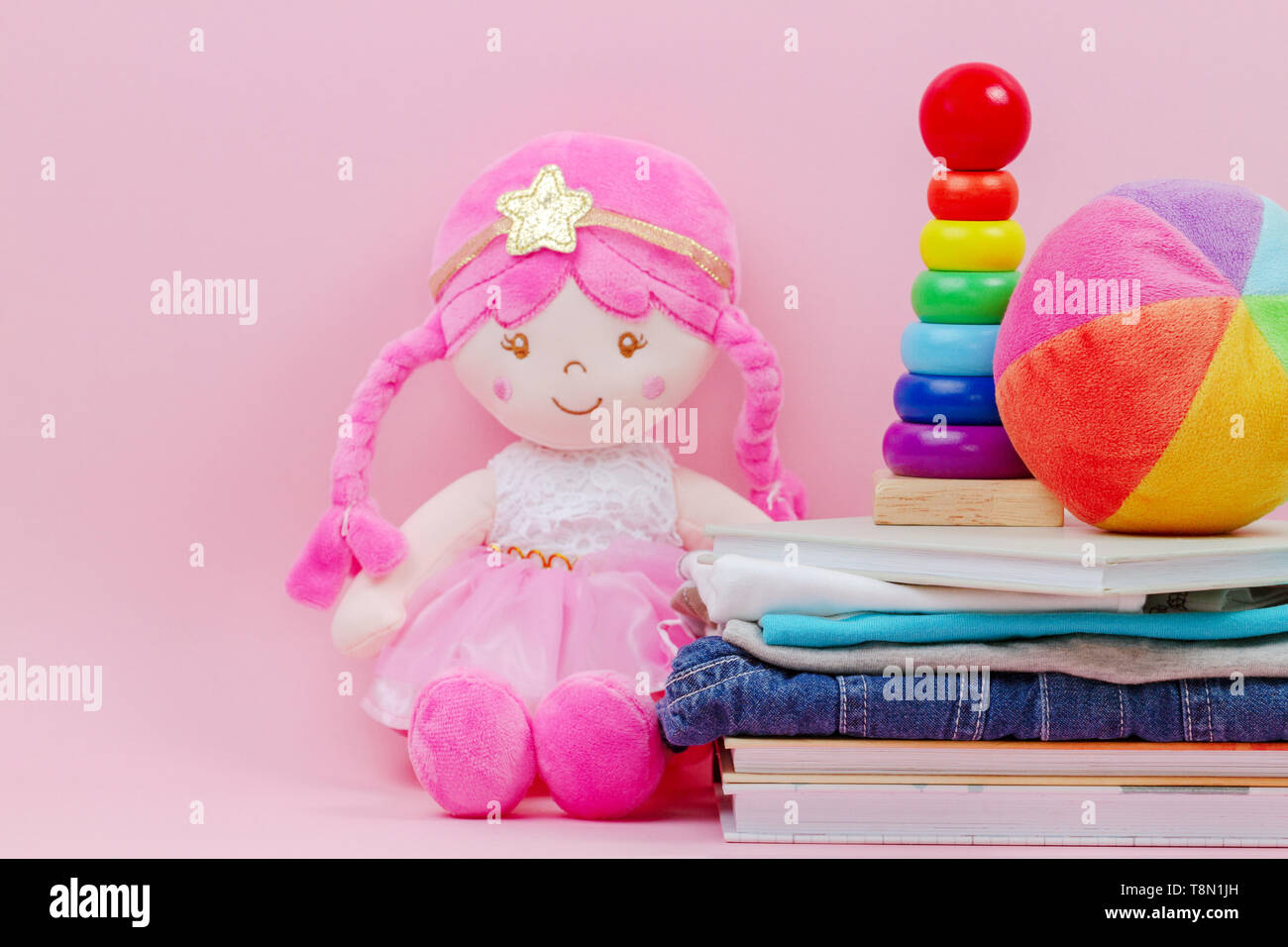 Donation, charity concept. Stuffed soft doll, baby stacking rings pyramid, kid clothes and books over pink background. Stock Photo
