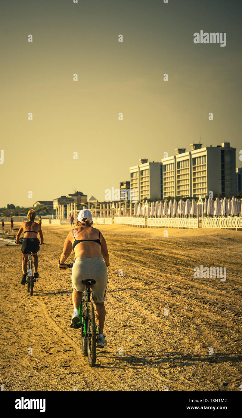 older women ride bikes along beach Stock Photo
