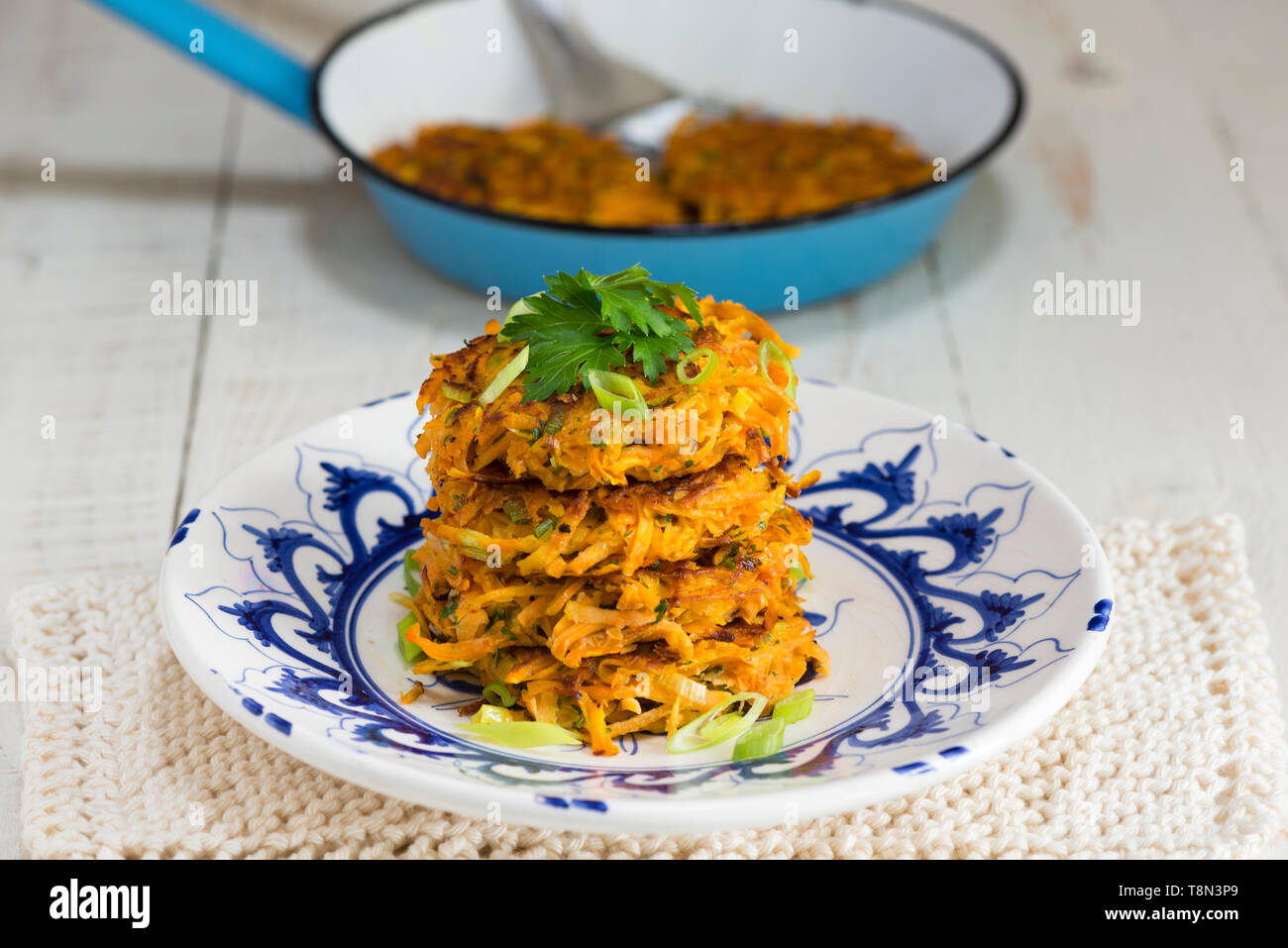 A stack of four sweet potato and carrot rostis on a blue and white plate. Stock Photo