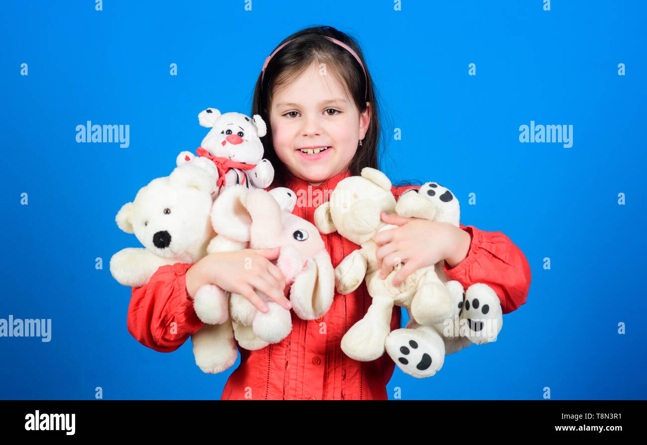 Little girl play with soft toy teddy bear. Lot of toys in her hands. Childhood concept. Collecting toys hobby. Cherishing memories of childhood. Small girl smiling face with toys. Happy childhood. Stock Photo