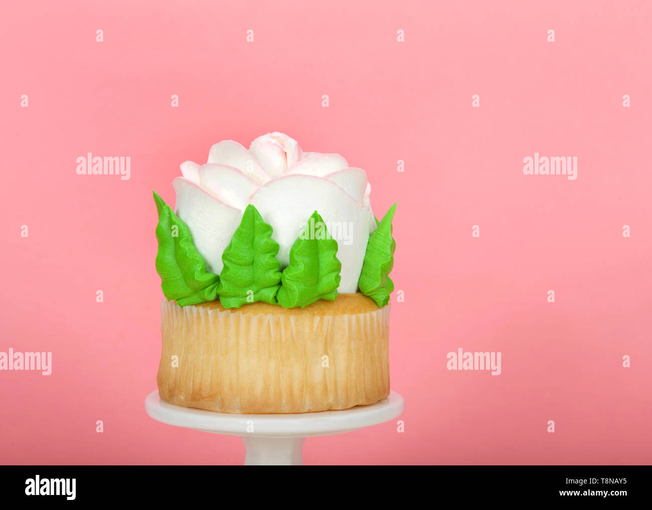 Close up on large cup cake with giant frosting rose sitting on white pedestal on wood table. Simple design with copy space for Mother's Day, Valentine Stock Photo