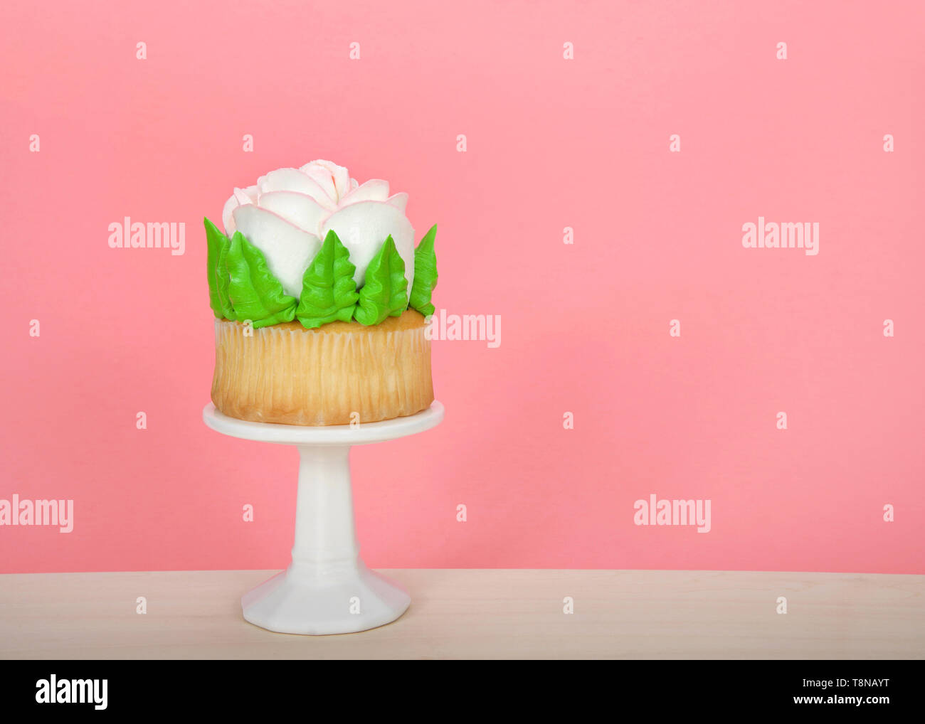 Large cup cake with giant frosting rose sitting on white pedestal on wood table. Simple design with copy space for Mother's Day, Valentine's Day, Quin Stock Photo