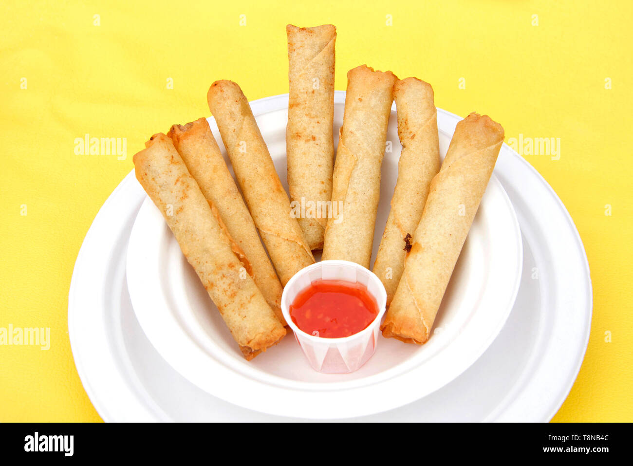 White paper plate with lumpia and dipping sauce on yellow table cloth. Popular street fair food. Stock Photo