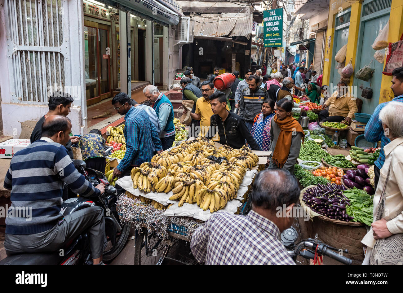 Men on motorbikes pass a fruit seller's car in a narrow street market,  Old City of Varanasi, India Stock Photo