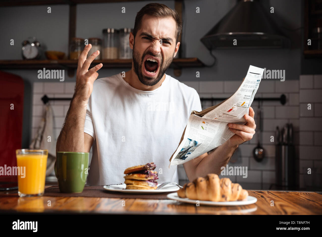 Angry shocked man having breakfast, reading newspaper Stock Photo