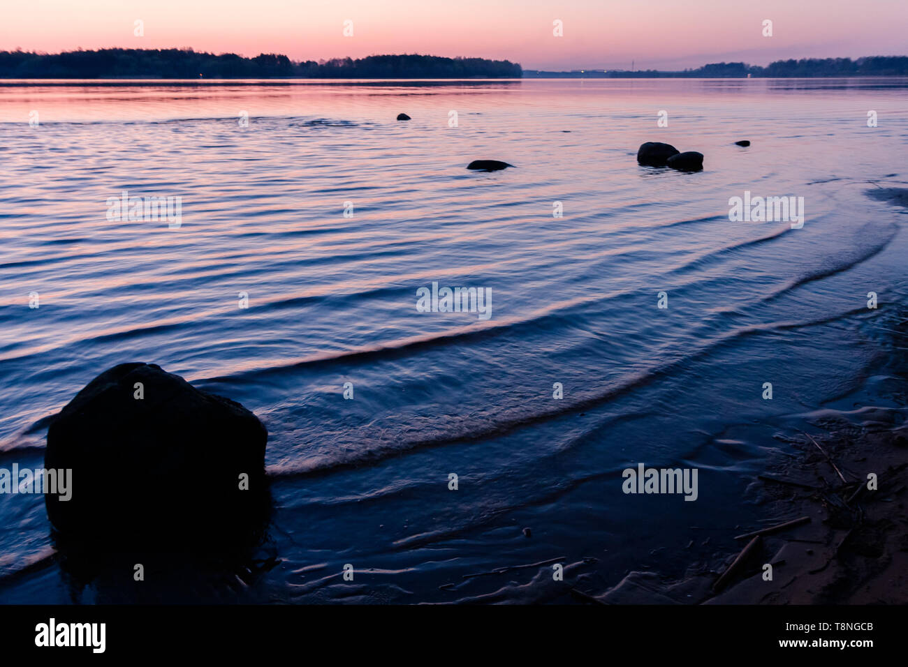 Relaxation landscape with a pink sunset on a wavy river and silhouettes of large stones - image Stock Photo