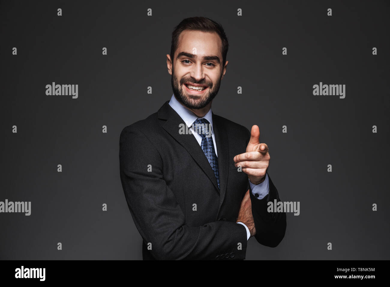 Portrait of a confident handsome businessman wearing suit isolated over black background, pointing finger at camera Stock Photo