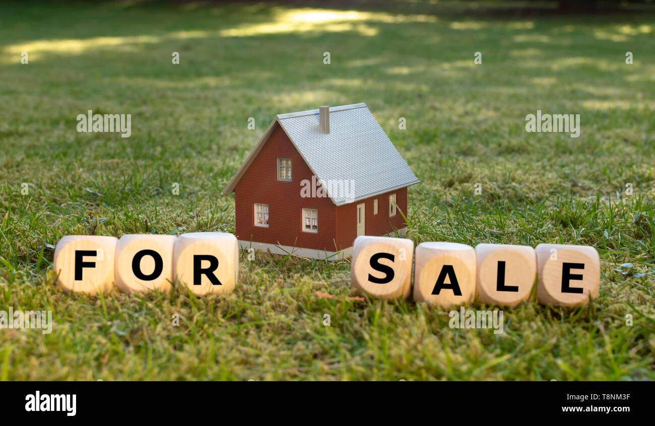 Cubes form the words 'for sale' in front of a miniature house. Stock Photo