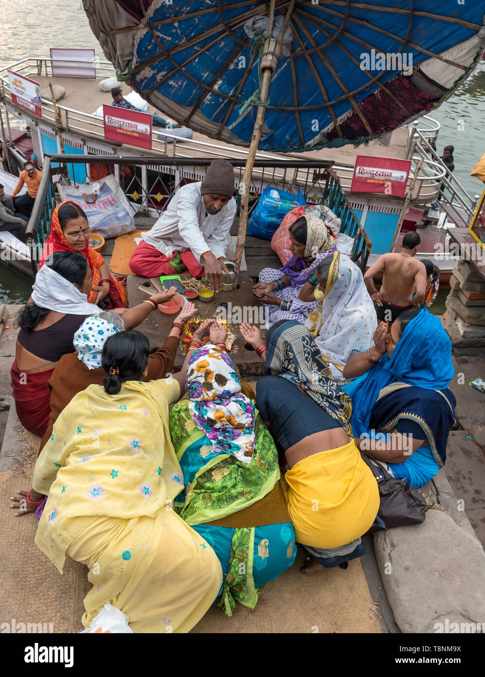 Group of women extend their hands to a priest by the River Ganges, Varanasi, India Stock Photo