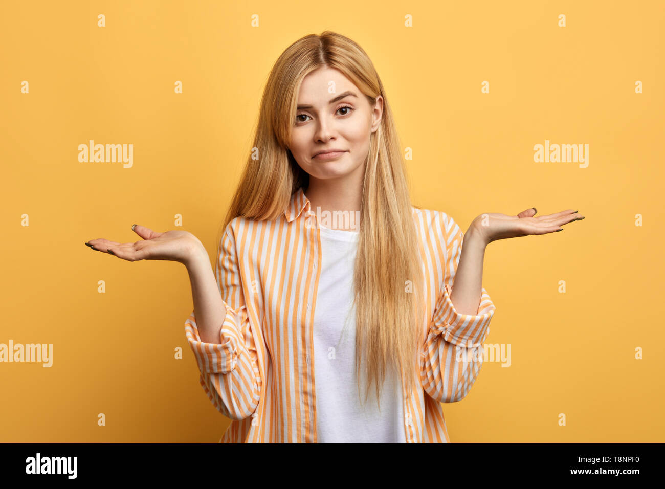Puzzled hesitant girl with long fair hair dressed casually, shrugs  shoulders as doesn t know answer, to be or not to  yellow  background Stock Photo - Alamy