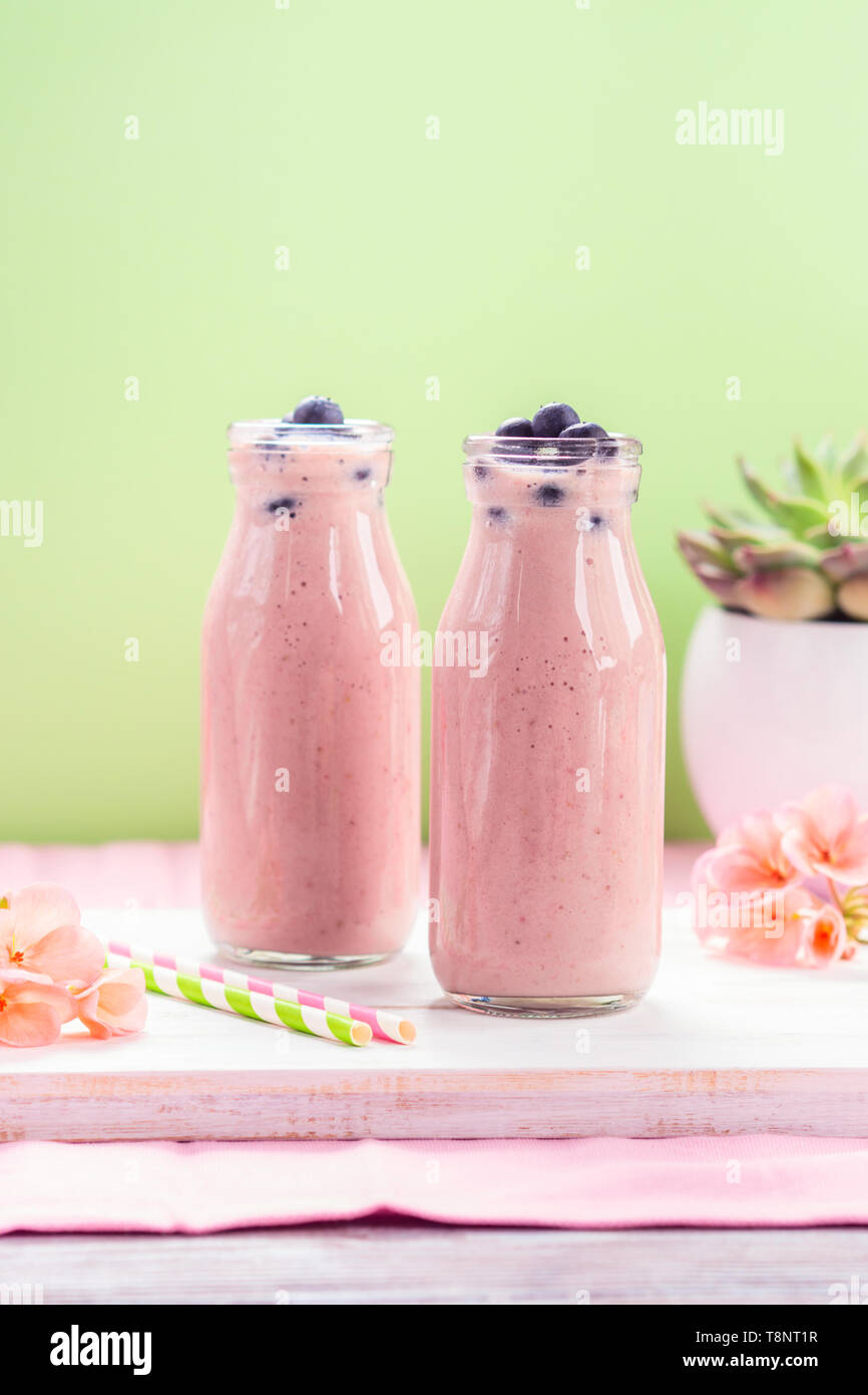 https://c8.alamy.com/comp/T8NT1R/pink-milk-shake-in-glass-bottles-topped-with-blueberries-pink-flowers-and-colorful-straws-T8NT1R.jpg