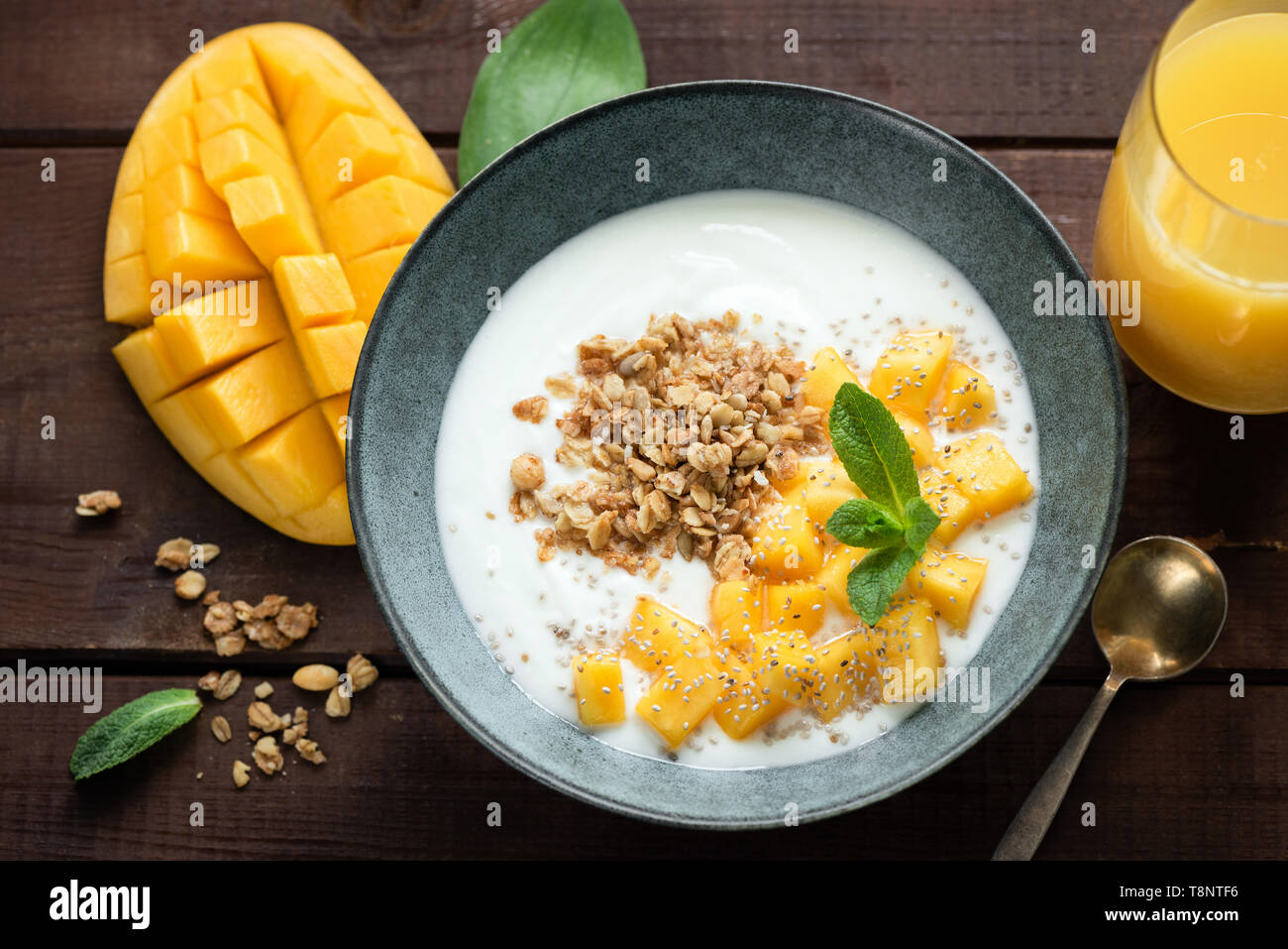 Breakfast yogurt bowl with mango and granola on a wooden table