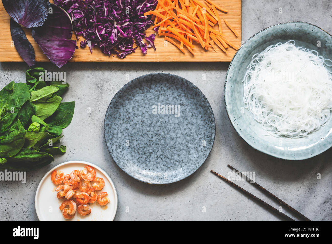 Healthy food preparation background. Asian cuisine food. Red cabbage, cucumber, glass rice noodles, spinach and shrimps. Top view. Grey concrete backd Stock Photo