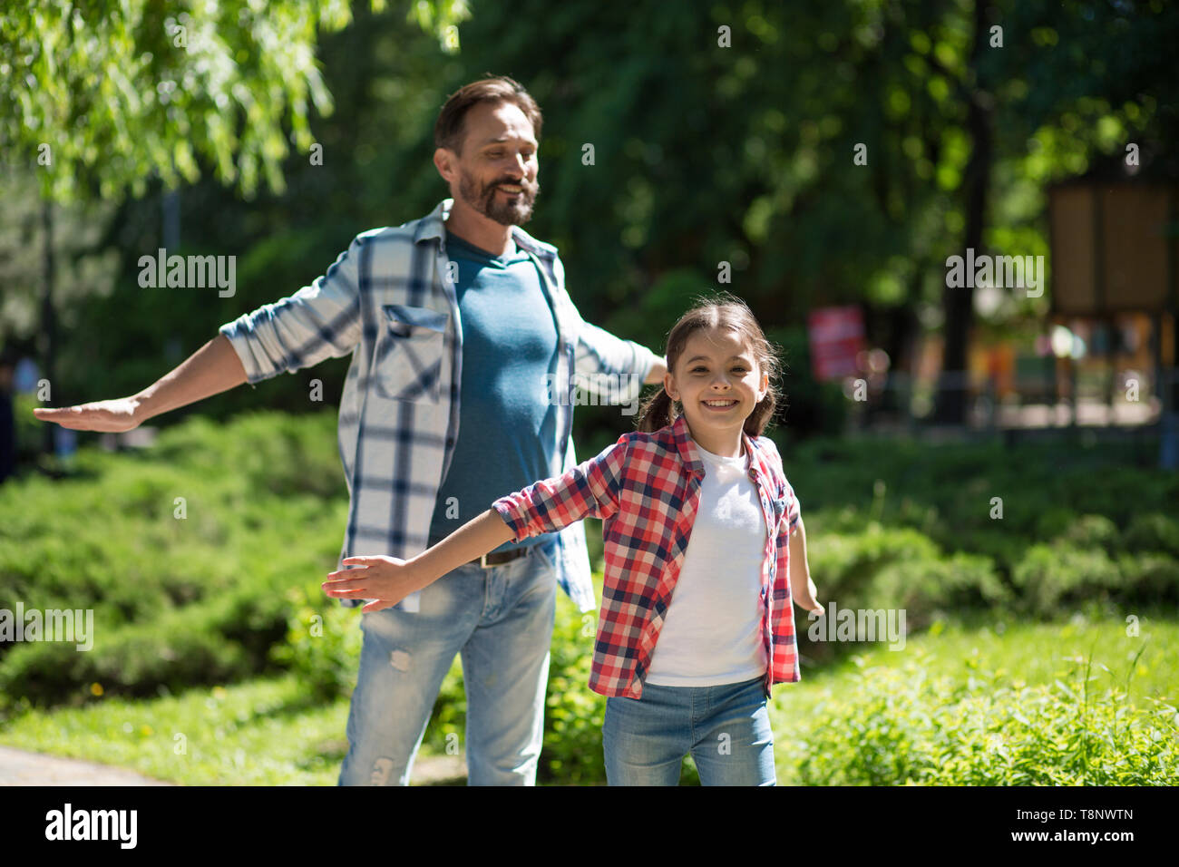 Father Spending Time with Daughter In The Park While Standind Whith Wild Opened Hands And Smiling. Stock Photo
