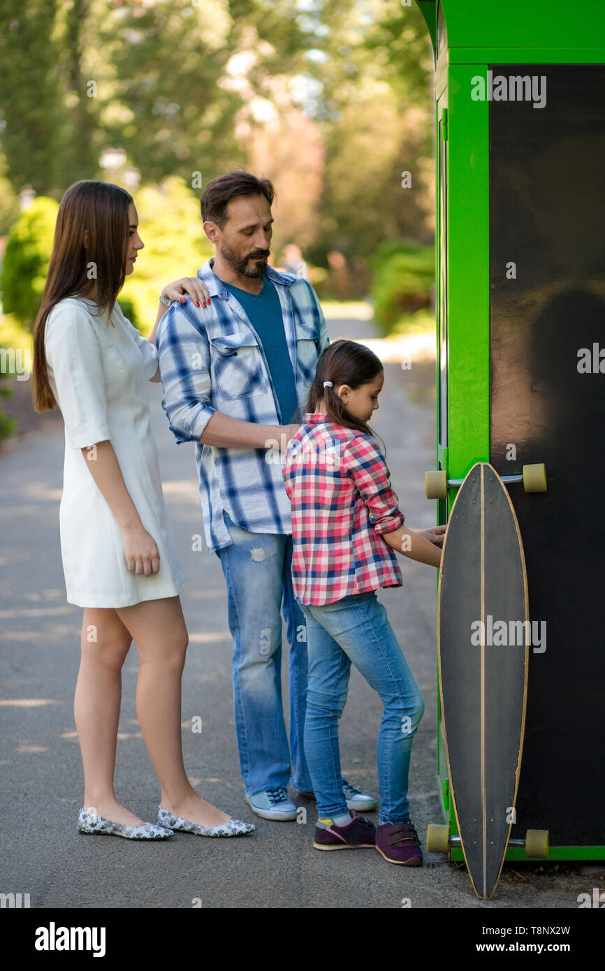 Family Spend Time In The Park While Standing Near Shop. The Skateboard Is By The Shop. Stock Photo