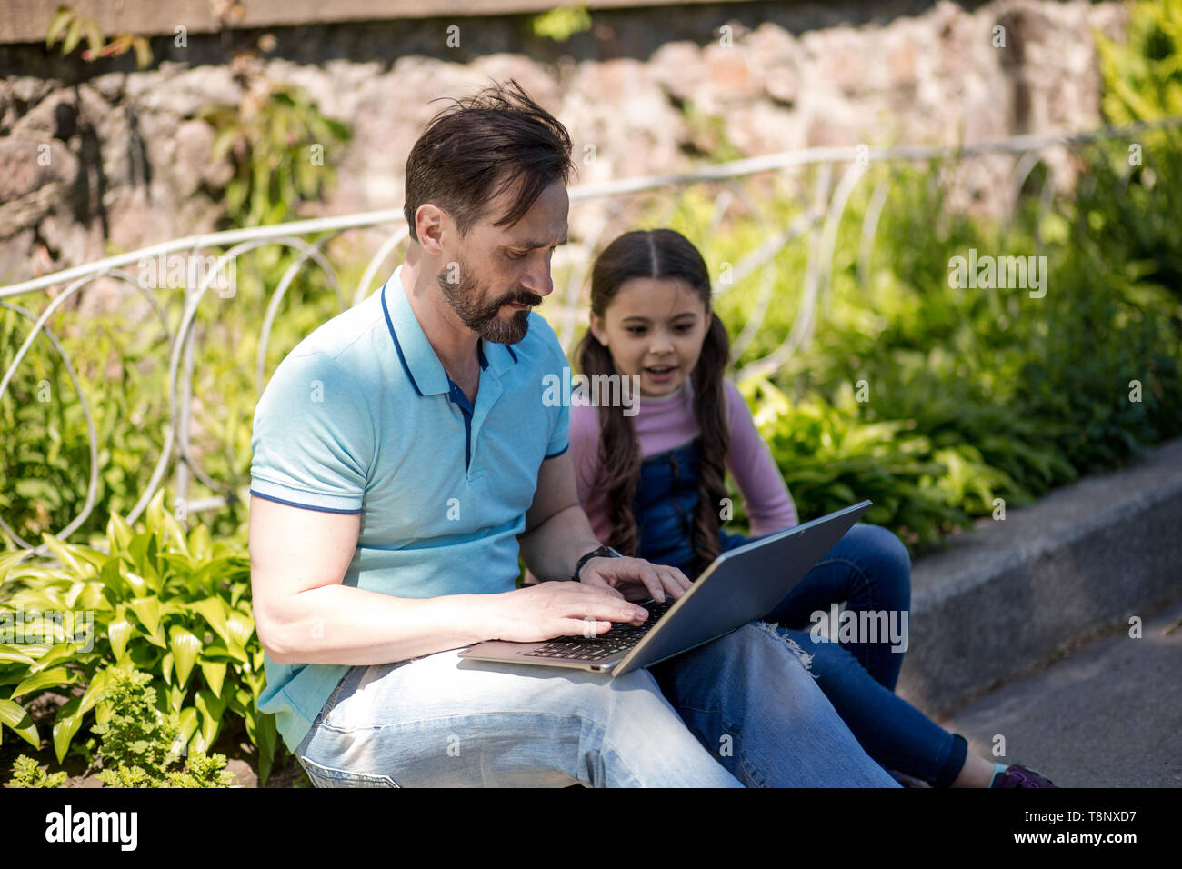 Father Siting Together With His Daughter And Looking On The Laptop Outdoors. Stock Photo