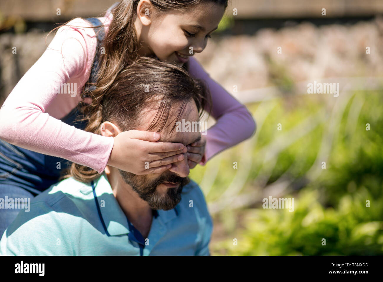 The Girl Is Closeing Her Dad's Eyes With Her Hands Outdoors. Stock Photo
