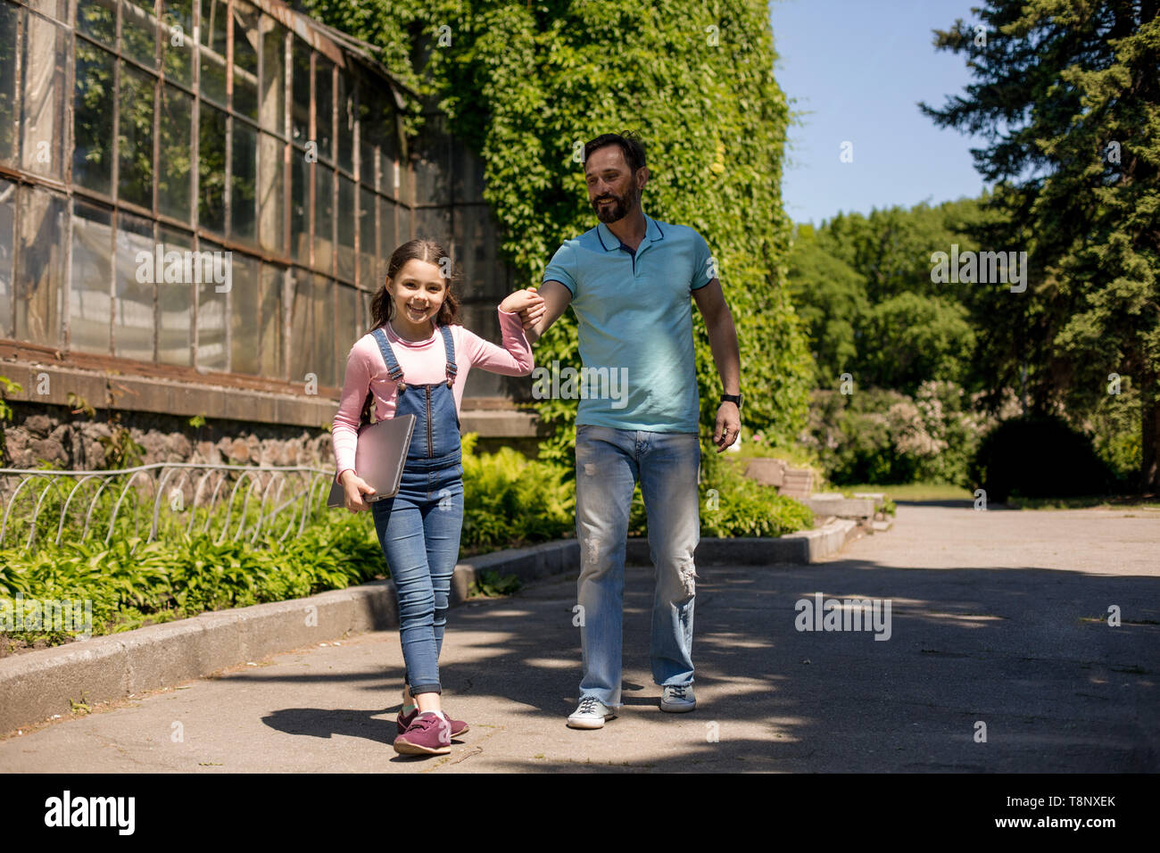 Daughter Is Leading Her Father While Holding Silver Laptop Outdoors. Stock Photo