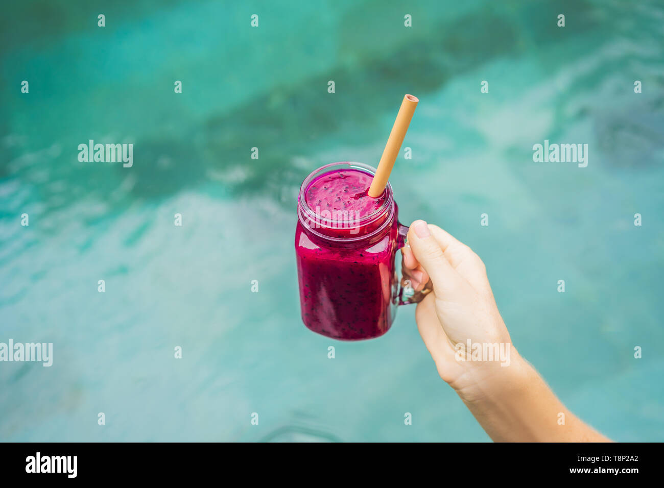 Young woman drinking Dragon fruit smoothies on the background of the pool. Fruit smoothie - healthy eating concept. Close up of detox smoothie with Stock Photo