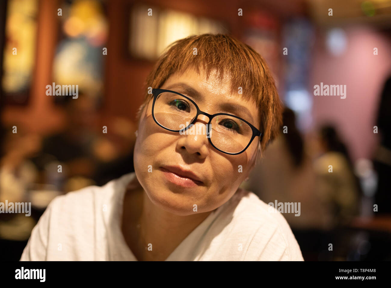 Mature Taiwanese woman of Chinese ethnicity sitting in a warm, cozy restaurant Stock Photo