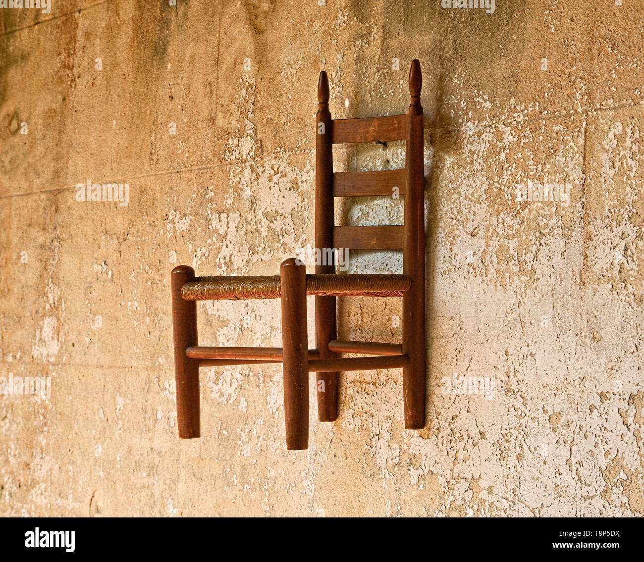 An old wooden chair hanging on a brown plaster wall Stock Photo Alamy