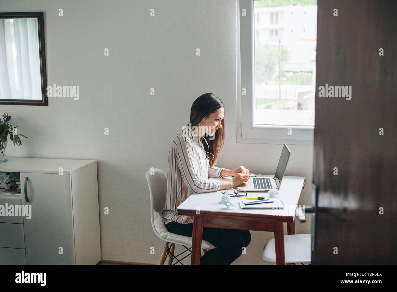 Girl in headphones works at the laptop in the home office and listens to music or a podcast. Stock Photo