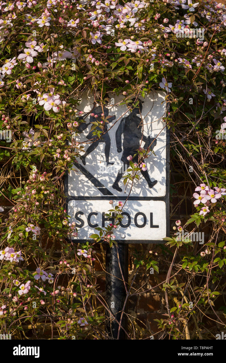 An old-fashioned school sign depicting a boy and girl off to school surrounded by clematis flowers in Turville. Stock Photo