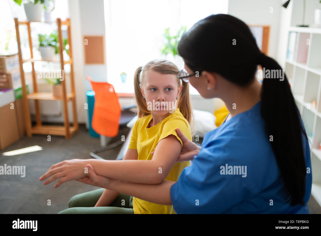 Scared blonde girl in yellow t-shirt sitting in medical cabinet Stock Photo