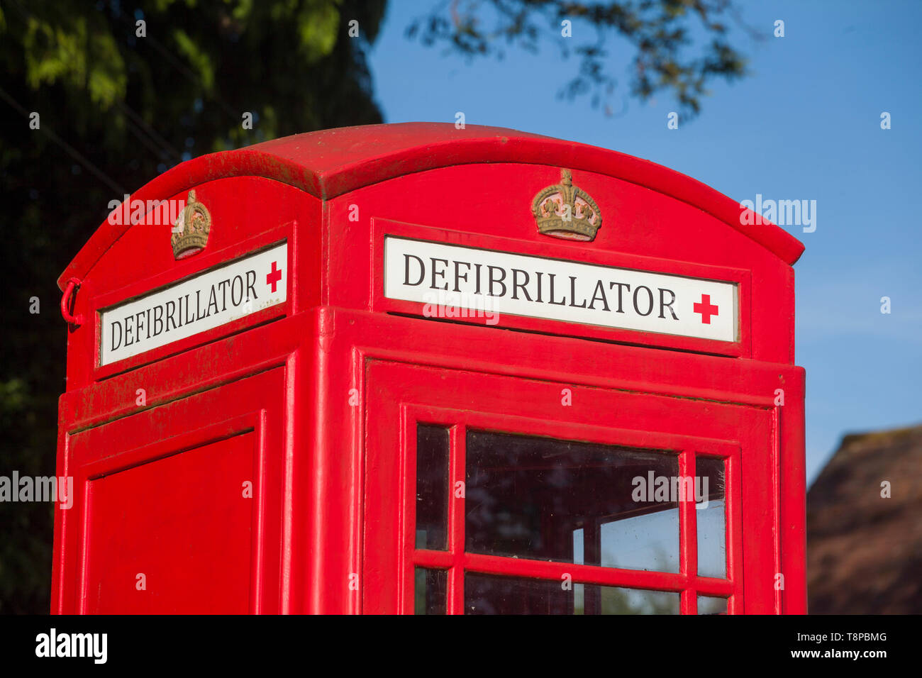 A bright red traditional public telephone box converted to house a community emergency defibrillator in Peppard Common, Oxfordshire Stock Photo