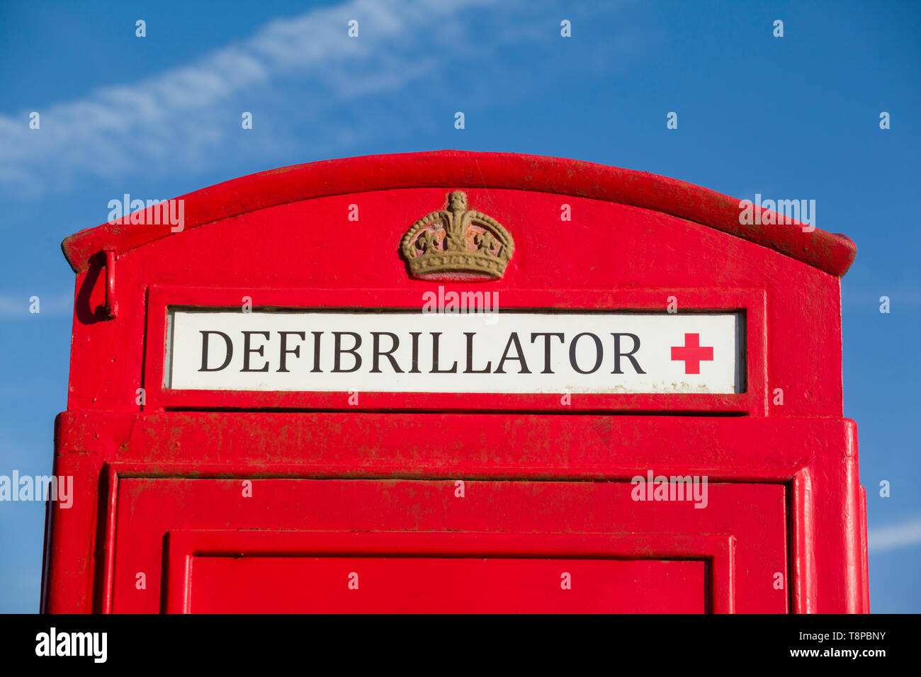 A bright red traditional public telephone box converted to house a community emergency defibrillator in Peppard Common, Oxfordshire Stock Photo