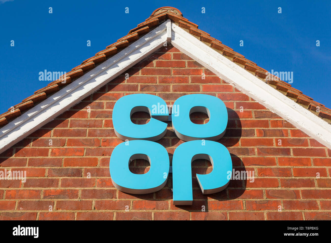 A brightly coloured Co-op sign against a blue sky on the gable end of one of their shops Stock Photo