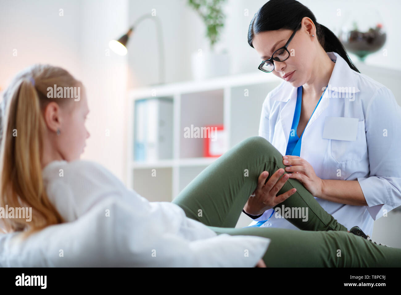 Concentrated experienced Asian therapist in clear glasses inspecting leg Stock Photo