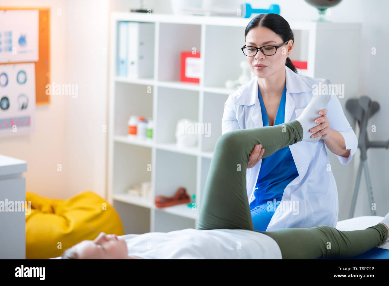 Accurate professional nurse moving problematic leg of little girl Stock Photo
