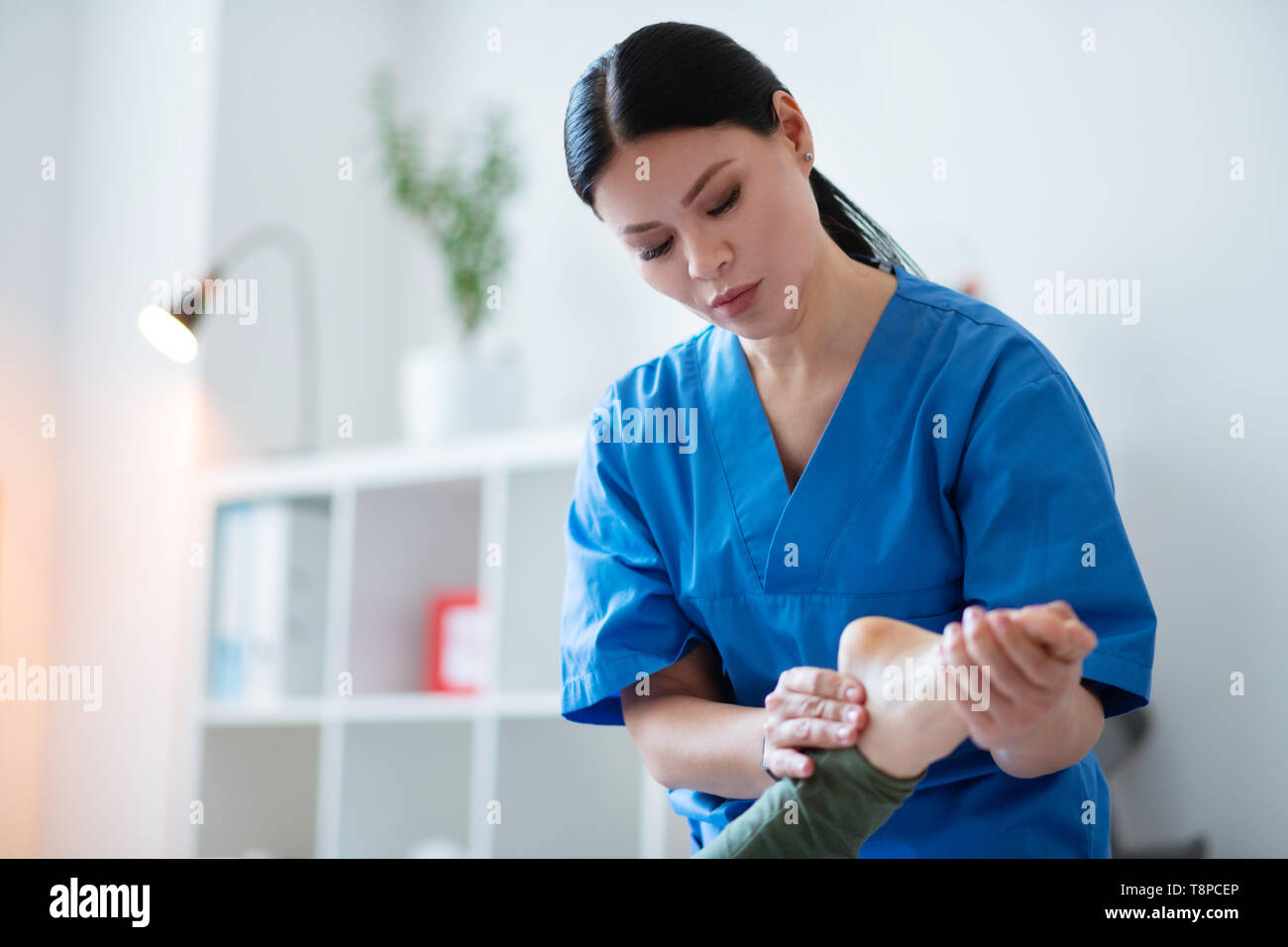 Focused long-haired woman in blue uniform doing leg massage Stock Photo -  Alamy