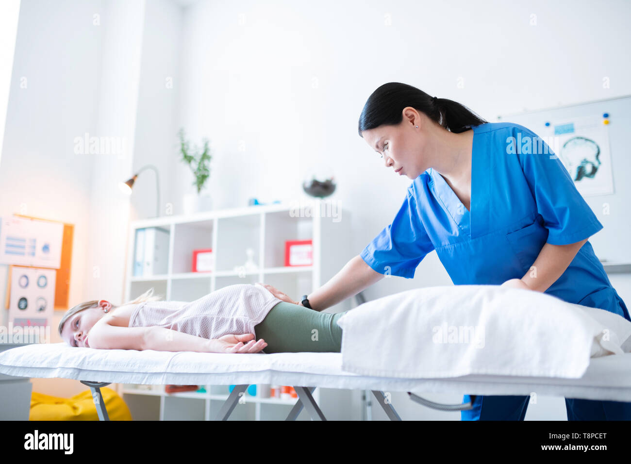 Experienced Asian therapist rubbing lying girl while staying in cabinet Stock Photo