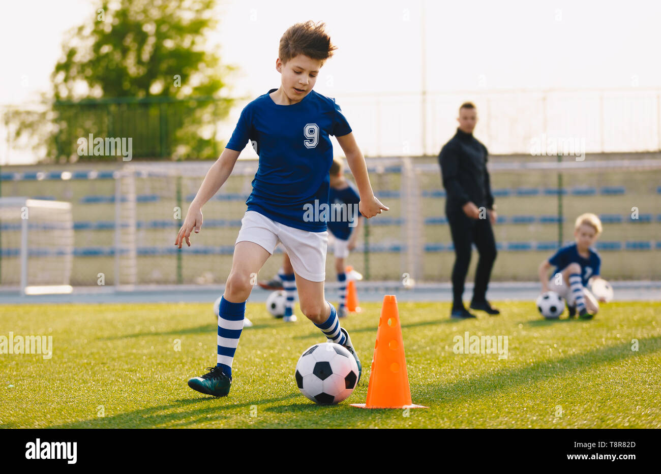 Boys training football dribbling in a field. Kids Running the Ball. Players develop soccer dribbling skills. Children training with balls and cones. S Stock Photo