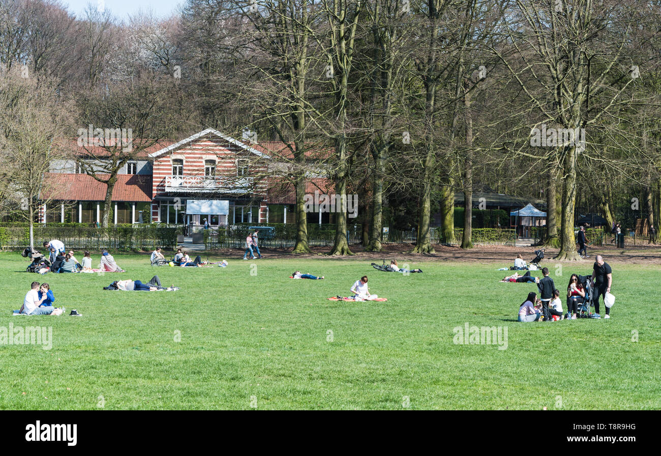 Ixelles, Brussels/ Belgium - 03 30 2019: Mixed group of people walking and restinging at the green lawns of the Bois de La Cambre city park during a s Stock Photo