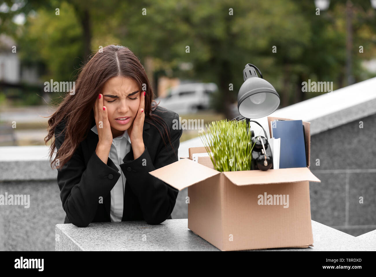 Fired stressed worker with personal stuff suffering from headache outdoors Stock Photo