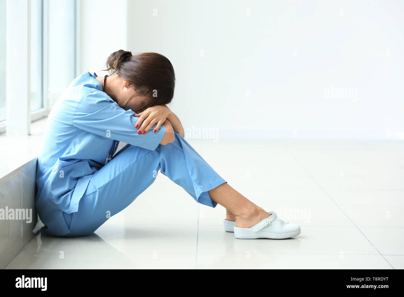 Tired female nurse sitting on floor in hospital Stock Photo Alamy