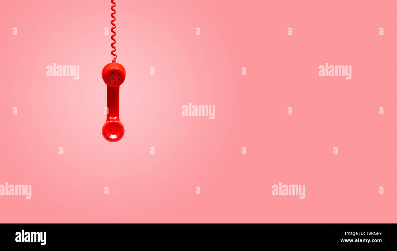 Red old telephone receiver hanging on pink background with texting space, waiting for phone call, vintage telephone. Stock Photo